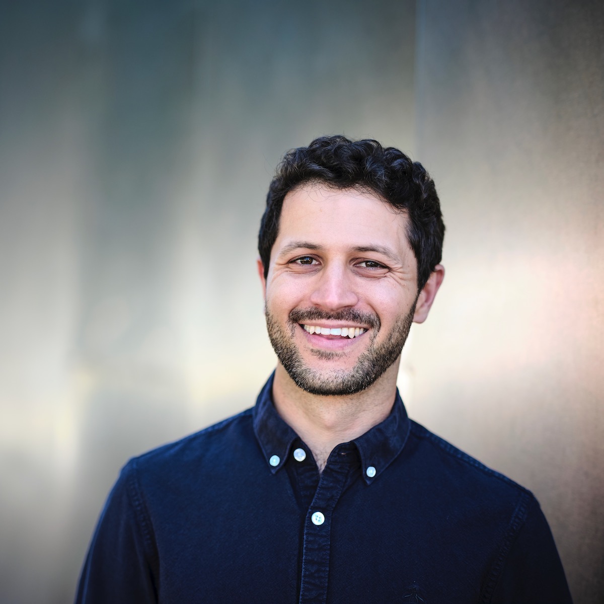 Joseph Bohigian smiling headshot in front of silver background.