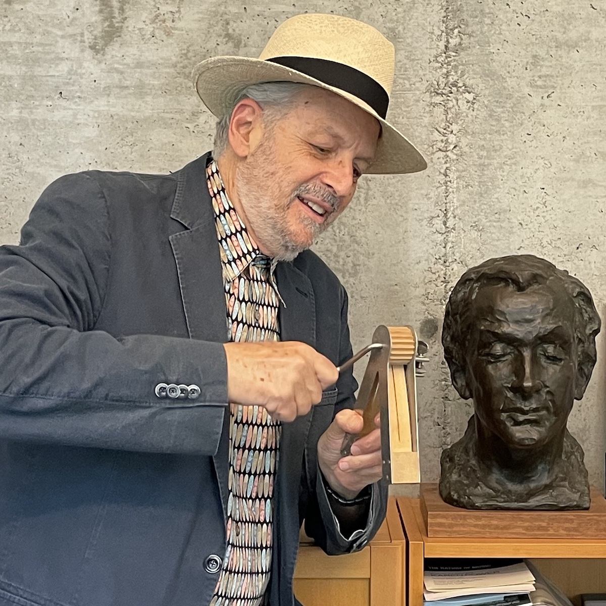 Charles Amirkhanian cranking a ratchet next to a bust of Henry Cowell.