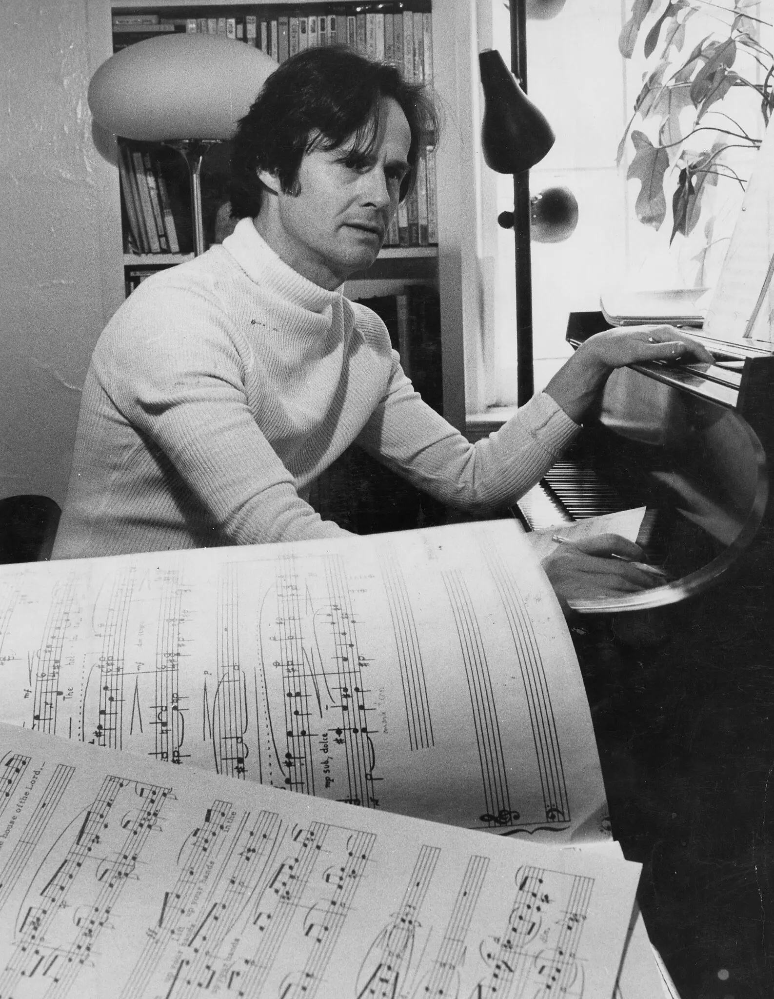 Ned Rorem sitting at the piano with scores in the foreground.