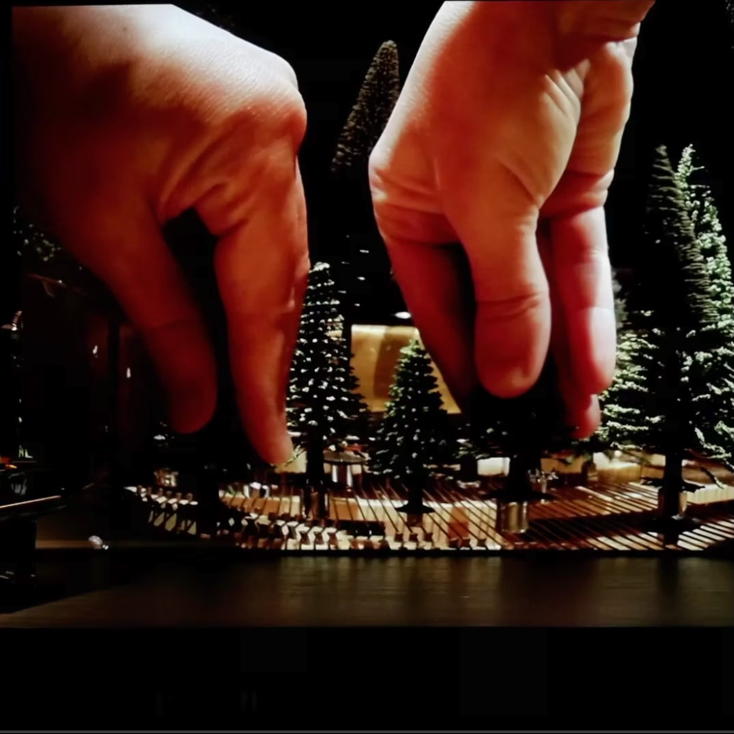 Two hands manipulating plastic trees inside a piano.