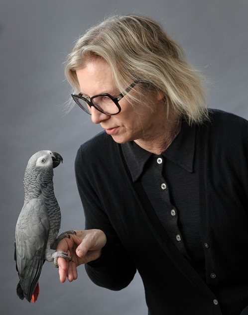 A woman wearing glasses holding a gray parrot.