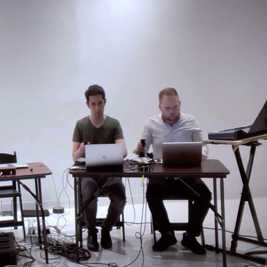 Two people sitting at a table with joysticks and laptops.