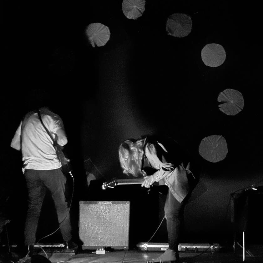 Black and white image of two people playing guitars with their faces obscured.