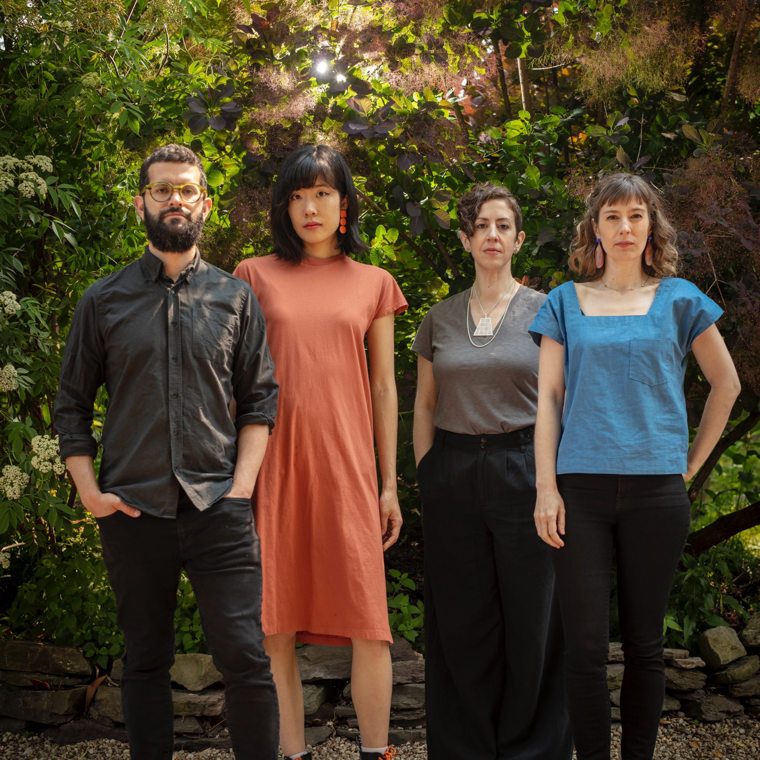 Four people standing in front of trees with green leaves.
