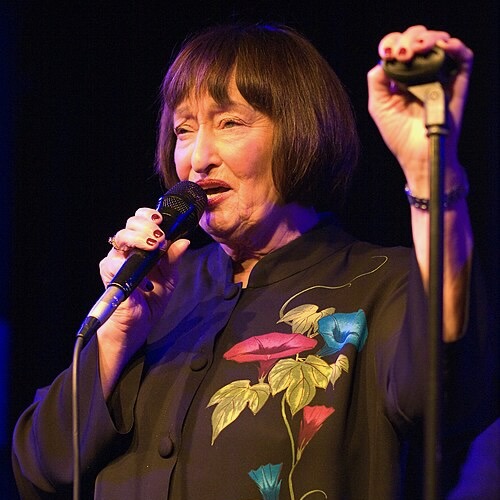 Sheila Jordan singing into a microphone, holding a microphone stand.