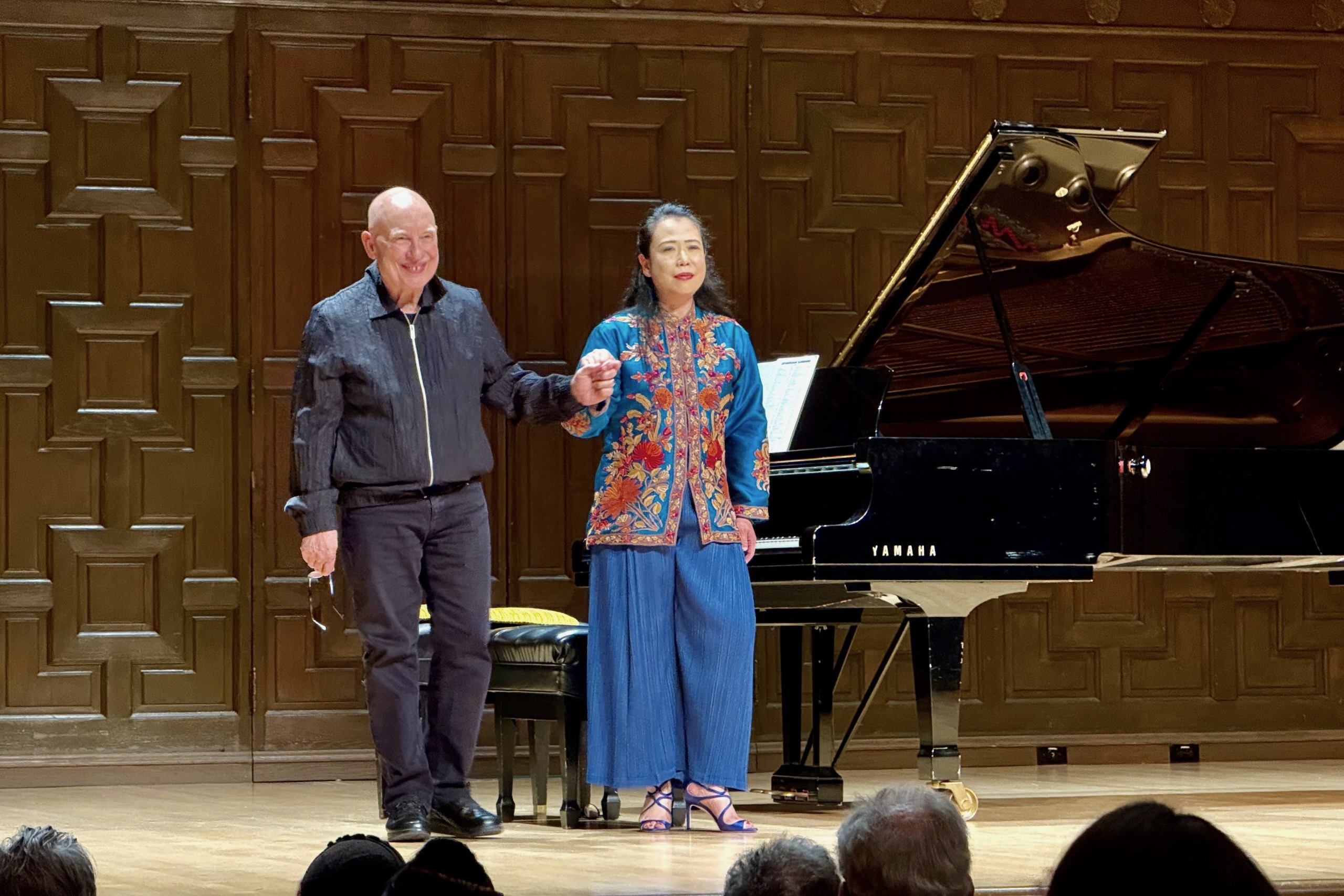 Dennis Russell Davies & Maki Namekawa A man and woman stand on stage with a grand piano. They are about to bow, they are accepting applause.