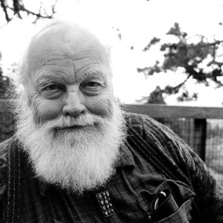Lou Harrison An older gentleman with a beard staring into the camera with a haunting smile.