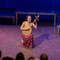 Jen Shyu playing a plucked string instrument and singing.
