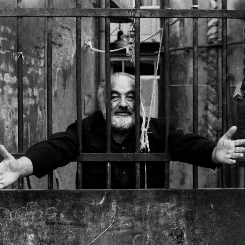 Sergei Parajanov with arms outstretched behind bars.